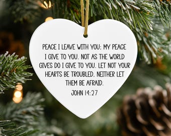May include: A white heart-shaped ceramic ornament featuring black printed text that reads: PEACE I LEAVE WITH YOU: MY PEACE I GIVE TO YOU. NOT AS THE WORLD GIVES DO I GIVE TO YOU. LET NOT YOUR HEARTS BE TROUBLED. NEITHER LET THEM BE AFRAID. JOHN 14:27.