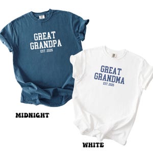 May include: A midnight blue t-shirt with white text reading GREAT GRANDPA EST. 2026 and a white t-shirt with dark blue text reading GREAT GRANDMA EST. 2026. Both shirts feature short sleeves and a crew neckline in a standard cotton fabric.