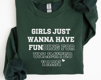 May include: A forest green long-sleeve crewneck sweatshirt featuring white block lettering that reads GIRLS JUST WANNA HAVE FUNDING FOR UNLIMITED YARN with a small white heart icon at the end of the text. The garment has a ribbed collar and cuffs.