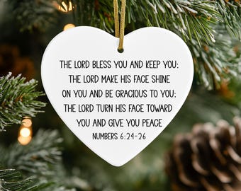 May include: A white heart-shaped ceramic ornament featuring black printed text that reads: THE LORD BLESS YOU AND KEEP YOU: THE LORD MAKE HIS FACE SHINE ON YOU AND BE GRACIOUS TO YOU: THE LORD TURN HIS FACE TOWARD YOU AND GIVE YOU PEACE NUMBERS 6:24-26.