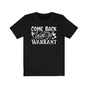 Peut inclure: T-shirt &agrave; manches courtes noire avec un texte blanc qui dit "Come Back With A Warrant" et deux petits c&oelig;urs.