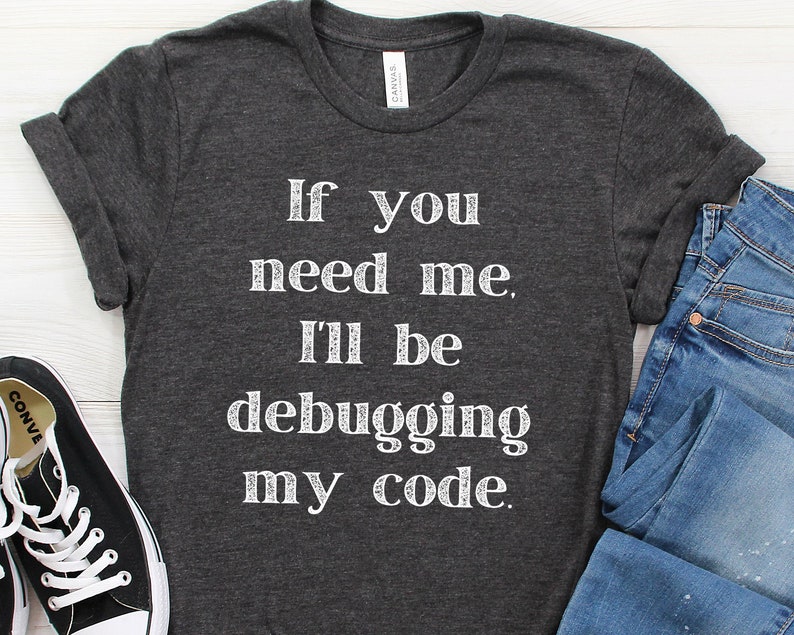 May include: A dark grey t-shirt with the text "If you need me, I'll be debugging my code." printed in white.