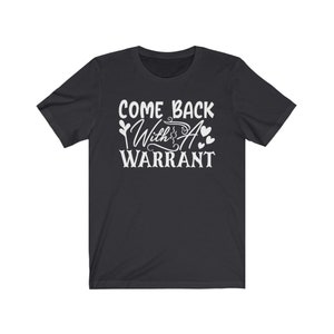 Peut inclure: T-shirt &agrave; manches courtes noire avec un texte blanc qui dit "Come Back With A Warrant" et un petit graphique en forme de c&oelig;ur.