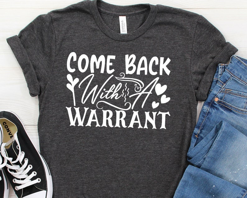 Peut inclure: Un t-shirt gris fonc&eacute; avec le texte "Come Back With A Warrant" en lettres blanches. Le texte est stylis&eacute; avec un c&oelig;ur et un graphique de plante.