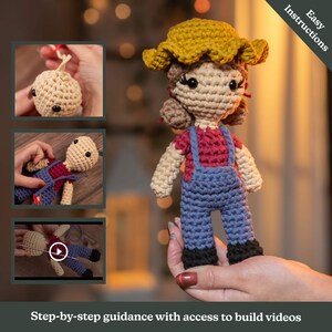 May include: Crochet doll with a yellow hat, red shirt, and blue overalls. The doll is being held by a hand. The image includes the text "Easy Instructions" and "Step-by-step guidance with access to build videos".