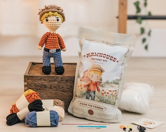 May include: Crochet kit for making a farmhouse-themed doll. The kit includes yarn in various colors, stuffing, crochet hooks, and instructions. The doll is named "Dixon the Farmer" and is wearing a red shirt, blue jeans, and a brown hat.
