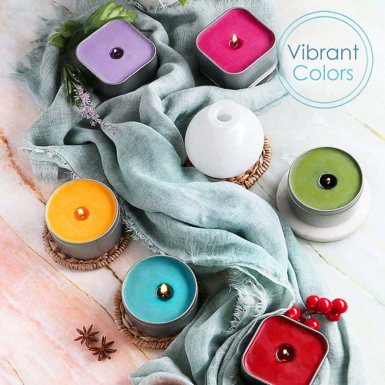 May include: Assortment of six candles in various colors, including purple, pink, yellow, green, blue, and red. The candles are in metal tins and are arranged on a light blue fabric and a white marble surface. The text "Vibrant Colors" is written in a blue circle.