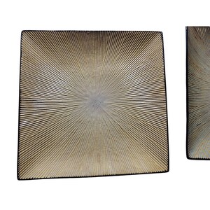May include: Two decorative wall panels with a sunburst design. The panels are square and rectangular, with a textured, metallic gold finish and black borders. The design radiates from a central point.