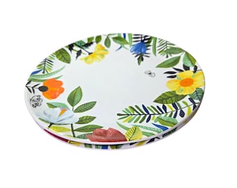 May include: White ceramic plate with a colorful floral design. The plate features a border of green leaves, yellow, orange, and red flowers. A small insect is also visible on the plate. The plate is approximately 10 inches in diameter.
