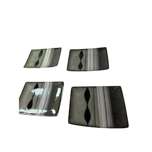 May include: Four rectangular ceramic plates with a unique design. Each plate features a central black, hourglass-shaped accent, complemented by vertical stripes in shades of gray, beige, and white. The plates have a dark green border.
