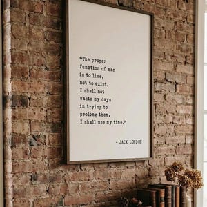 May include: A rectangular framed wall art piece featuring a white background with black typewriter-style text that reads: The proper function of man is to live, not to exist. I shall not waste my days in trying to prolong them. I shall use my time. - JACK LONDON.