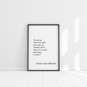 May include: A framed print with a black border, featuring a quote by Ralph Waldo Emerson in a typewriter font. The quote reads, "Do not go where the path may lead, go instead where there is no path and leave a trail."