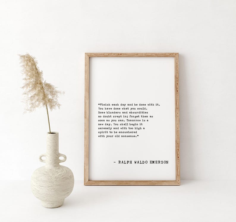 May include: A framed print with a quote by Ralph Waldo Emerson in black text on a white background. The frame is light brown. A decorative vase with a dried plant is to the left of the frame.