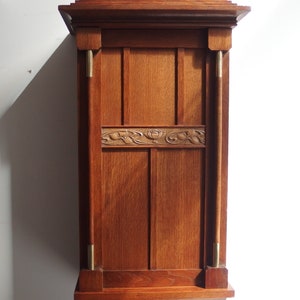 May include: A dark wood wall cabinet with a carved floral design and brass accents. The cabinet has a simple, rectangular shape and a shelf on the bottom.