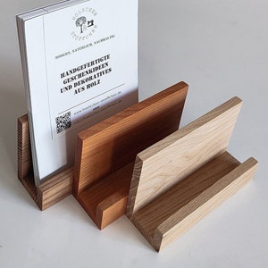 Könnte beinhalten: Ein Holz-Zeitschriftenständer mit drei Fächern. Der Ständer ist aus hellem und dunklem Holz gefertigt. Das obere Fach enthält eine Broschüre mit dem Text "Handgefertigte Geschenkideen und Dekoratives aus Holz" und einer Website-Adresse.