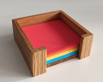 May include: Wooden desk organizer with a rectangular shape, holding a stack of colorful sticky notes. The organizer is made of light brown wood and has a simple, modern design. The sticky notes are red, orange, yellow, and blue.