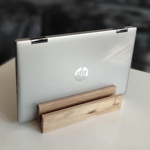 Könnte beinhalten: Ein silberner Laptop mit einem HP-Logo auf der Rückseite steht auf einem Holzständer. Der Ständer ist aus hellbraunem Holz mit natürlicher Maserung.