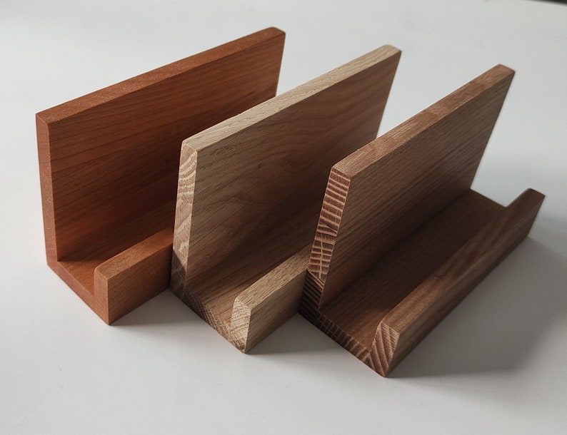 May include: Three wooden display stands, one is a light brown, one is a medium brown, and one is a dark brown. The stands are all made of wood with a natural finish.