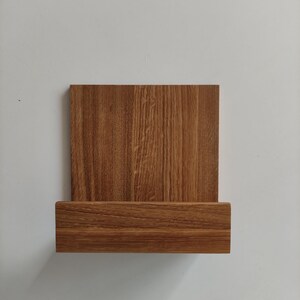 May include: A wooden wall shelf with a rectangular top and a lower shelf. The shelf is made of light brown wood with a wood grain pattern.