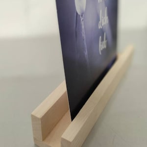 K&ouml;nnte beinhalten: Ein Holzbildst&auml;nder mit einer hellen Holzoptik. Der St&auml;nder hat einen Schlitz, um ein Bild oder eine Karte zu halten. Die Karte im St&auml;nder hat einen blauen Hintergrund mit einer wei&szlig;en Mohnkapsel und dem Text "hab dich lieb".