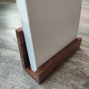 May include: A wooden book stand with a white book resting on top. The stand is made of dark brown wood and has a simple design.