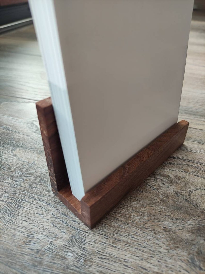 May include: A wooden book stand with a white book resting on top. The stand is made of dark brown wood and has a simple design.