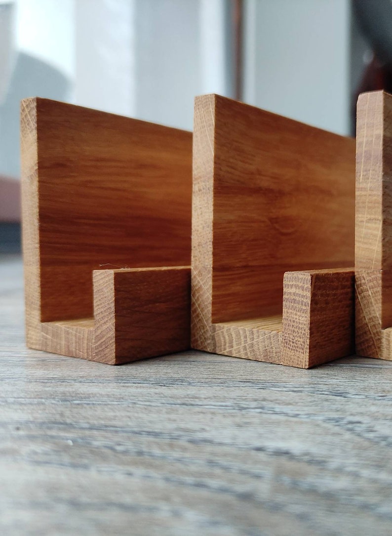 May include: Three wooden shelves with a natural finish, each with a U-shaped opening. The shelves are arranged in a row and are made of a light brown wood.