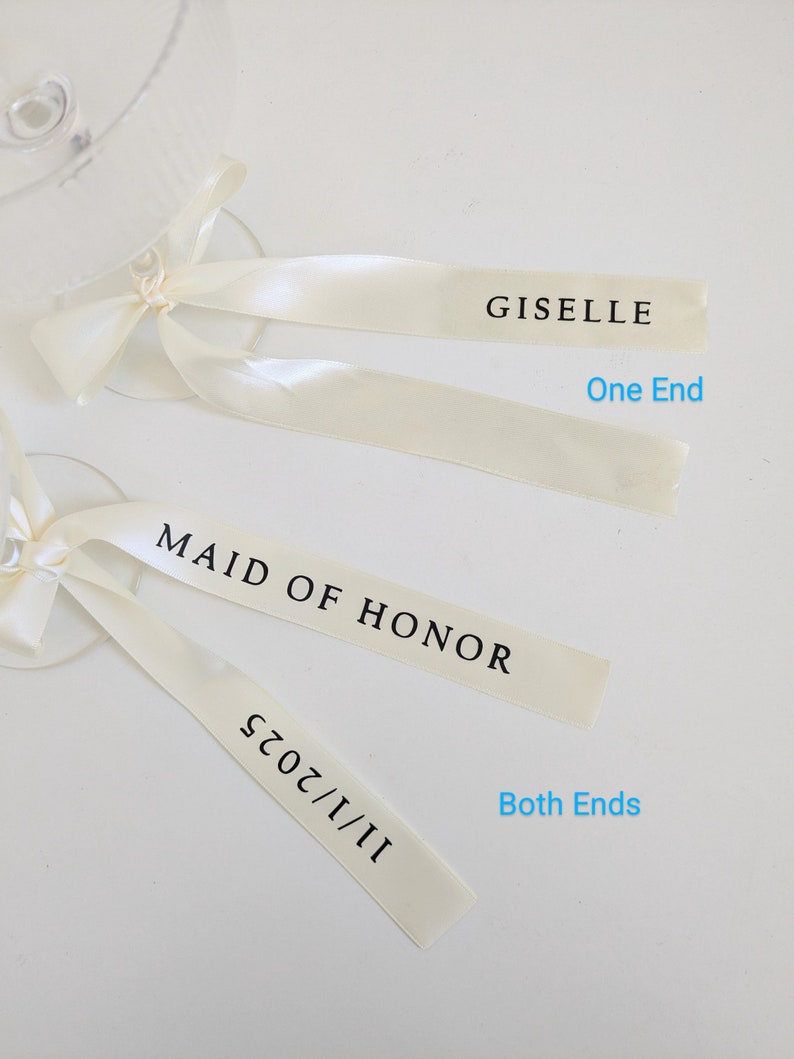 May include: Two cream-colored satin ribbons tied to glass stems. The top ribbon features the text GISELLE on one end. The bottom ribbon features the text MAID OF HONOR and 11/1/2025 on both ends. The text One End and Both Ends is visible.