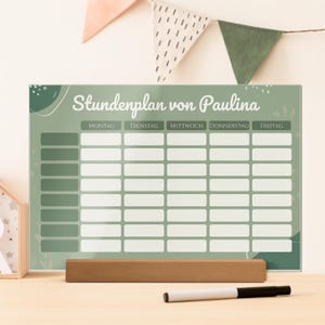 Könnte beinhalten: Eine grüne und weiße Wochenplan-Tafel mit dem Text "Stundenplan von Paulina" oben. Die Tafel hat ein Raster für jeden Wochentag. Ein Holzsockel und ein schwarz-weißer Marker befinden sich vor der Tafel.
