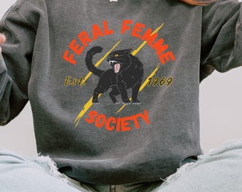 May include: A gray sweatshirt with a black cat graphic and the text "Feral Femme Society Est. 1969" in orange.