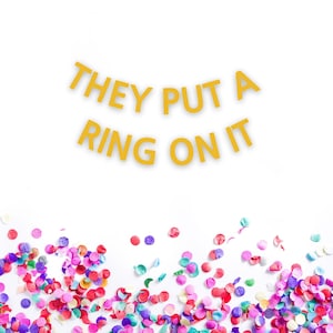 May include: A white background with the text "They put a ring on it" in gold letters. The bottom of the image is covered in colorful confetti.