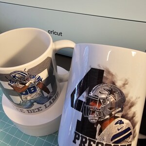 May include: Two white ceramic mugs with images of Dallas Cowboys football players. One mug features a player in a blue jersey with the number 88 and the name "Cee Dee Lamb". The other mug features a player in a blue jersey with the number 4 and the name "Prescott".