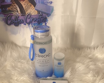 May include: A set of three CÎROC Vodka bottles, one large bottle and two smaller bottles. The bottles are clear glass with a blue label and a blue cap. The label says "CÎROC Vodka" and "Snap Frost Distilled from Fine French Grapes". The bottles are on a white fluffy surface.