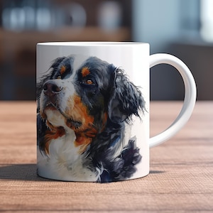 Könnte beinhalten: Ein weißer Keramikbecher mit einer detaillierten Aquarell-Illustration eines Berner Sennenhundes. Der Hund hat schwarzes, weißes und braunes Fell, eine weiße Blesse im Gesicht und braune Augen, die nach oben gerichtet sind.