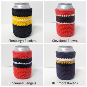 May include: Four crocheted can coolers in team colors. The coolers are black and yellow, red and brown, red and black, and purple and gold. Each cooler has a white stripe.