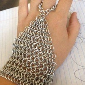 Peut inclure: Un bracelet et une bague en maille de chaîne argentés. Le bracelet est composé d'anneaux métalliques entrelacés et couvre le poignet et une partie de la main. La bague est attachée au bracelet et peut être portée sur n'importe quel doigt.