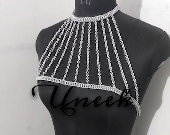 May include: Silver chainmail body jewelry with a choker style neckline and a decorative design. The jewelry is displayed on a black mannequin.