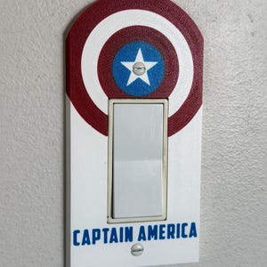 Peut inclure: Un cache-interrupteur sur le thème de Captain America. Le design présente le bouclier emblématique en rouge, blanc et bleu, avec une étoile blanche sur un cercle bleu. Les mots "CAPTAIN AMERICA" sont imprimés en bleu.
