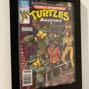 May include: A Teenage Mutant Ninja Turtles comic book cover featuring the four turtles in action poses. The cover is framed in black and has the title "Teenage Mutant Ninja Turtles Adventures" and the issue number "No. 1".