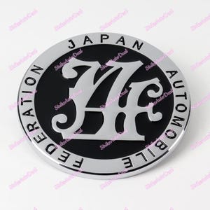 May include: A silver and black round emblem with the text "JAPAN AUTOMOBILE FEDERATION" surrounding a stylized "JAF" logo.