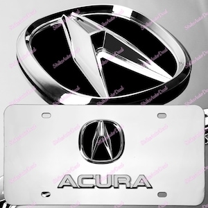 May include: A silver metal license plate frame with a chrome Acura logo and the word "ACURA" in raised lettering. The frame is designed to fit a standard US license plate.