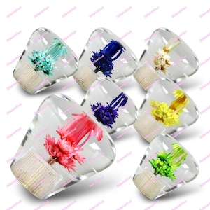 May include: A collection of clear, triangular bottle stoppers, each containing a different colored dried flower arrangement. Colors include blue, pink, yellow, green, and white. The stoppers have a light-colored, textured base.