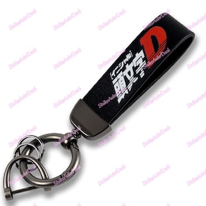 May include: Black leather keychain with a silver metal ring and a white graphic that says "Initial D" in Japanese. The letter "D" is red.