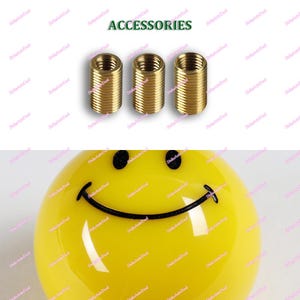Op de afbeelding: Drie messingkleurige schroefdraadfittingen worden weergegeven boven een gele smiley. Het woord "ACCESSORIES" is in het groen boven de fittingen gedrukt. De smiley heeft zwarte ogen en een gebogen zwarte mond.