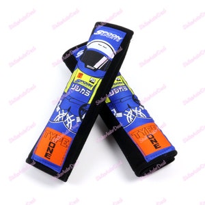 May include: Two black and blue car seat belt pads with a cartoon race car driver design. The pads have the text "Type One" and "Spoon Sports" printed on them.