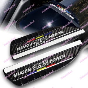 以下が含まれることがあります： 黒のカーボンファイバー製の車のドアサイドミラーカバー2つ。白い文字で「MUGEN POWER」と書いてあり、赤、黄、青、白のグラフィックが描かれている。