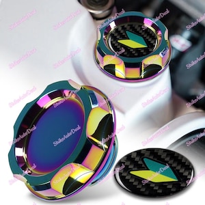 May include: Two iridescent oil caps with a black and yellow arrow design. The caps are made of metal and have a rainbow finish. The caps are designed to fit most standard oil fill openings.