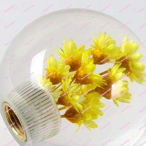 Puede incluir: Pomo de cambio de cristal transparente con un racimo de flores amarillas en su interior. La base del pomo es blanca con detalles dorados.