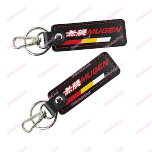 May include: Two black leather keychains with the word "MUGEN" in red and white, and Japanese characters. The keychains have a red, yellow, and white stripe design. Each keychain has a silver clasp and ring.