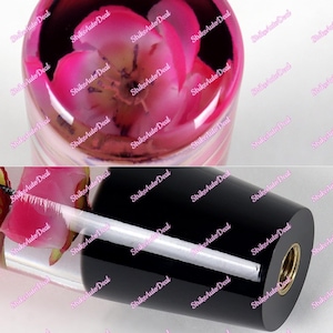 Peut inclure: Pommeau de levier de vitesse de voiture cylindrique transparent avec une fleur rose encapsulée dans de la résine. La base est noire et possède un insert fileté doré. La section supérieure montre la fleur en détail.